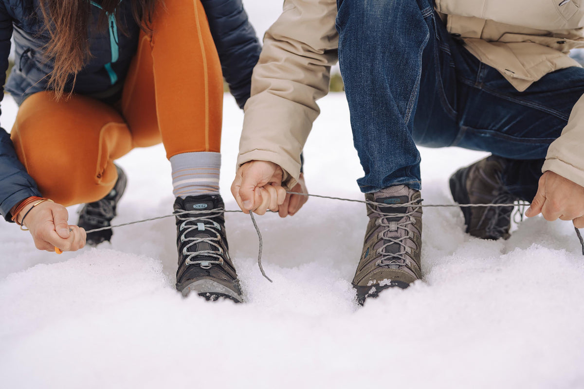 two people kneeling in snow and tying their warm winter boots