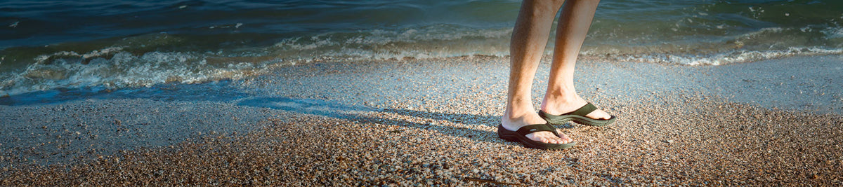 A pair of feet wearing KEEN flip flops at the beach.