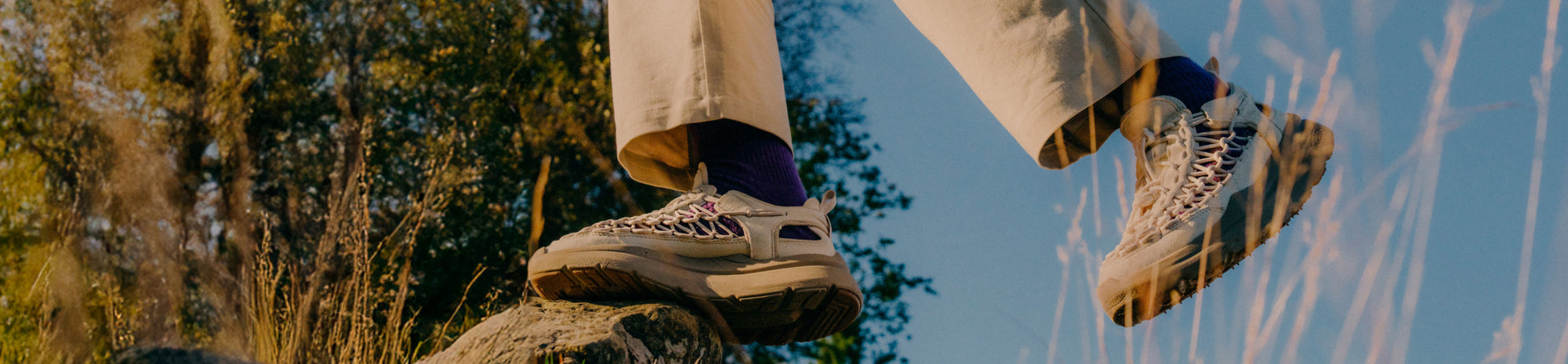 Banner image of a man and a woman walking along a stone path outside, wearing KEEN footwear