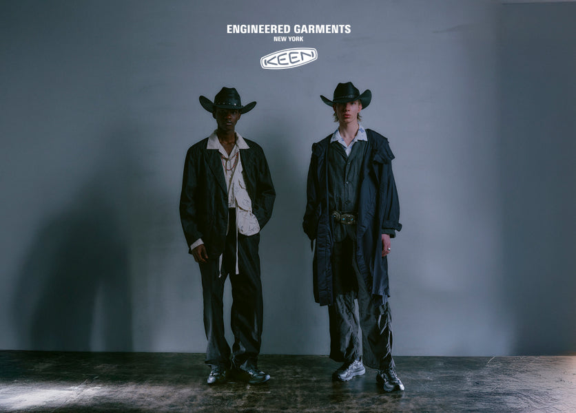 Two men wearing long black jackets, sneakers, and cowboy hats.
