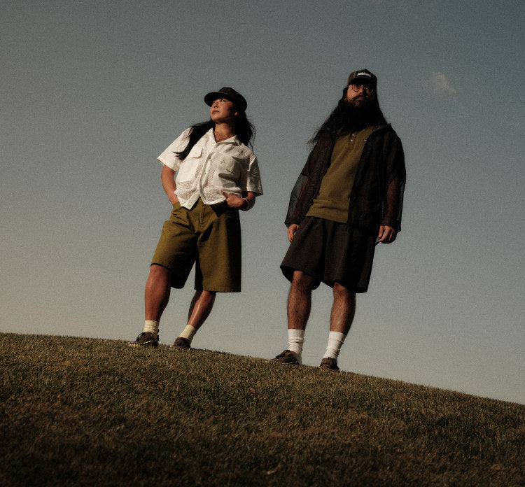 Two people standing on top of a grassy hill, wearing neutral tones.