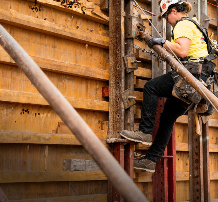 A construction worker climbing a ladder on a job site, wearing a tool belt and protective gear.
