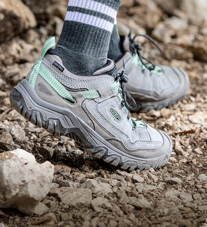 A person wearing grey and mint green KEEN hiking shoes outside.