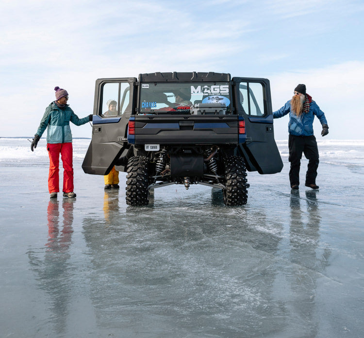 Two people standing next to a black off-road utility vehicle on a vast, frozen lake under a clear sky.