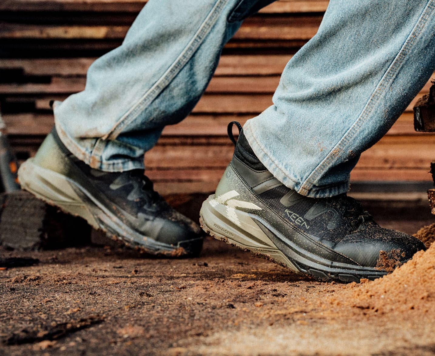 A man in jeans wearing black Targhee Blur utility boots and walking though lumberyard ground covered in wood shavings and dust. 