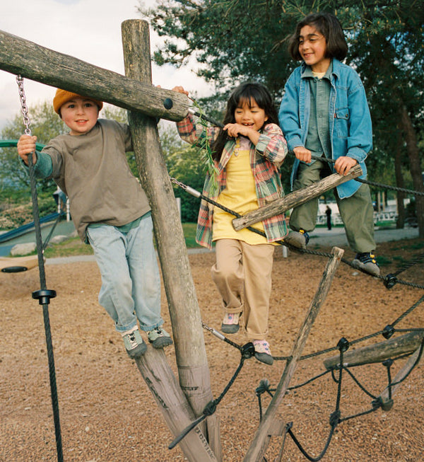 Three kids climbing on playground rope structure wearing close toed keen sneakers and sandals