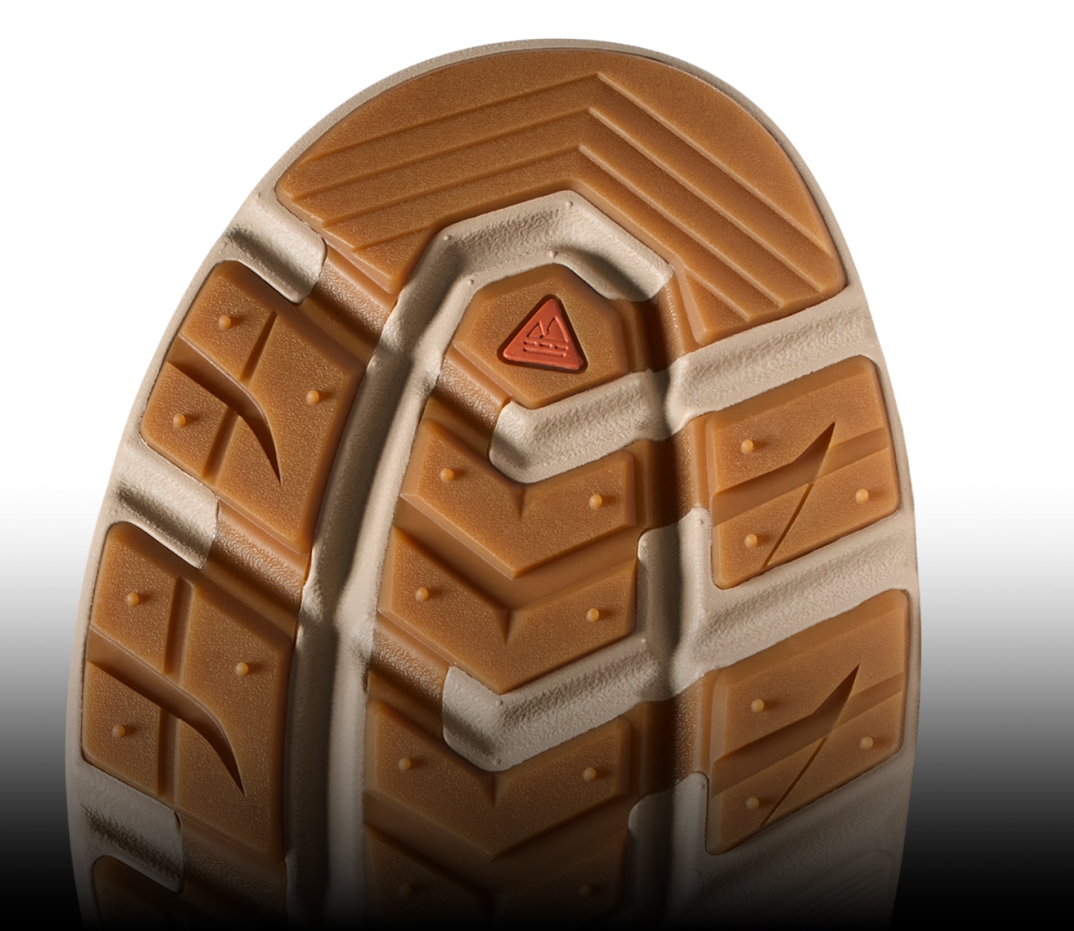 Close-up of a rugged tan shoe outsole with a triangular orange logo and aggressive traction lugs.