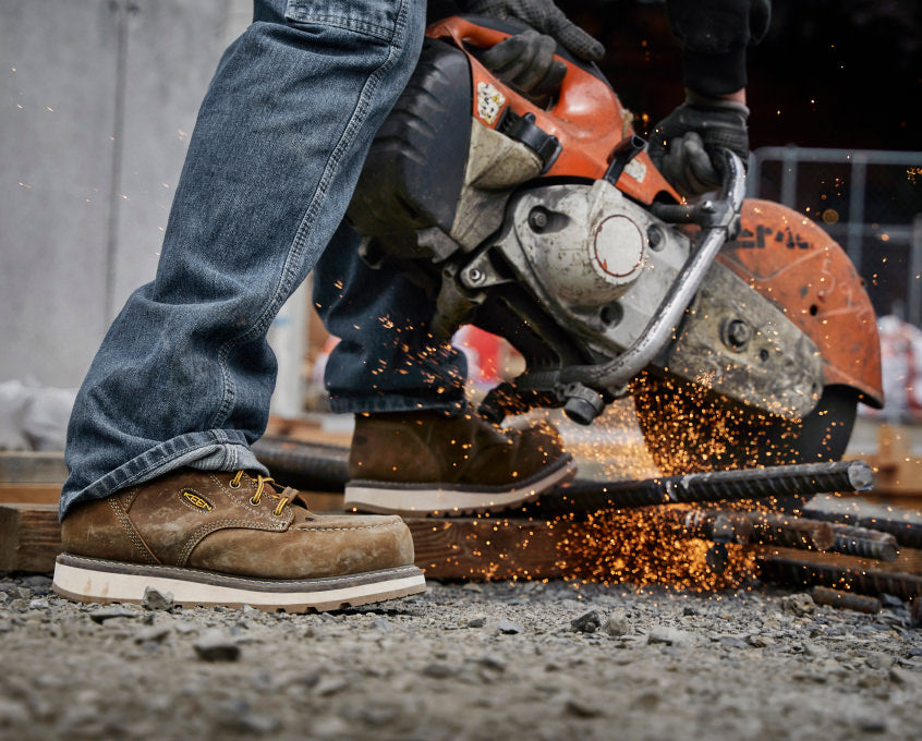 Knee down view of man wearing Cincinnati work boots and using a circular saw to cut metal 