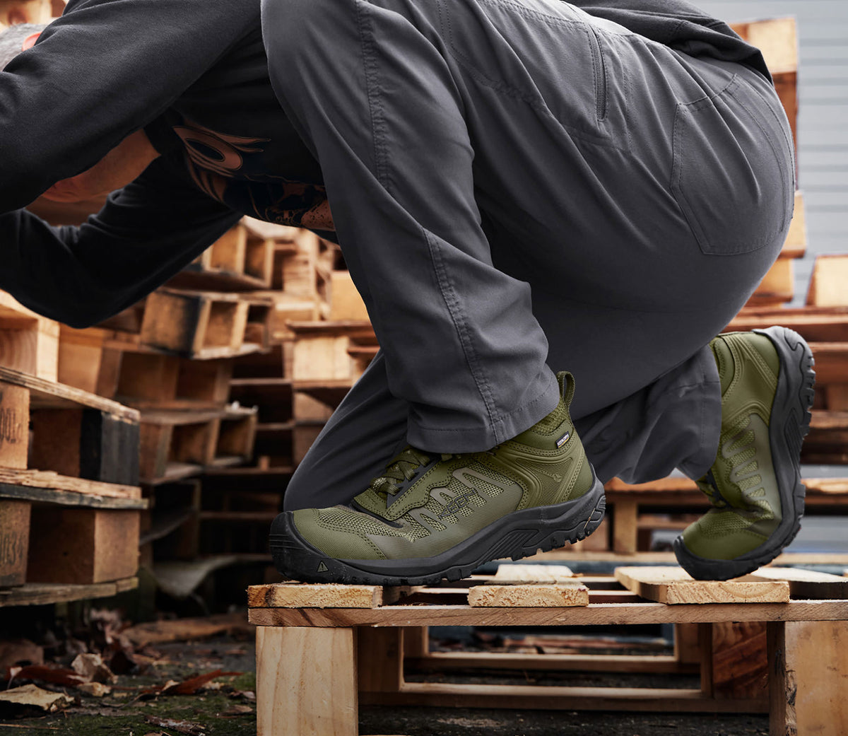 Man crouching down on wooden palette whearing green Reno work shoes
