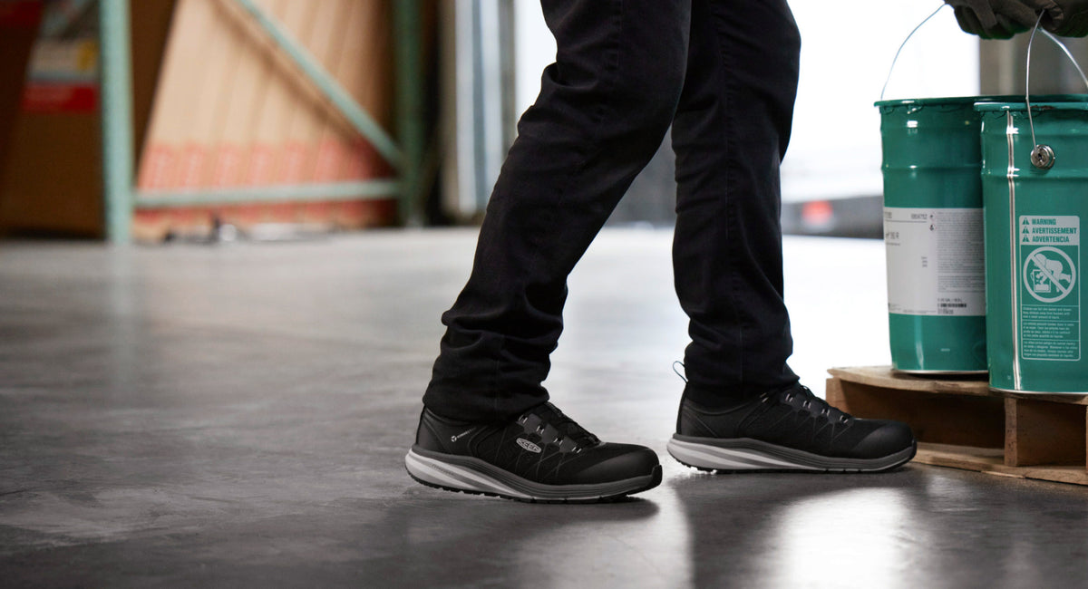 Knee down view of man wearing Vista Energy work sneakers and picking up two gren buckets