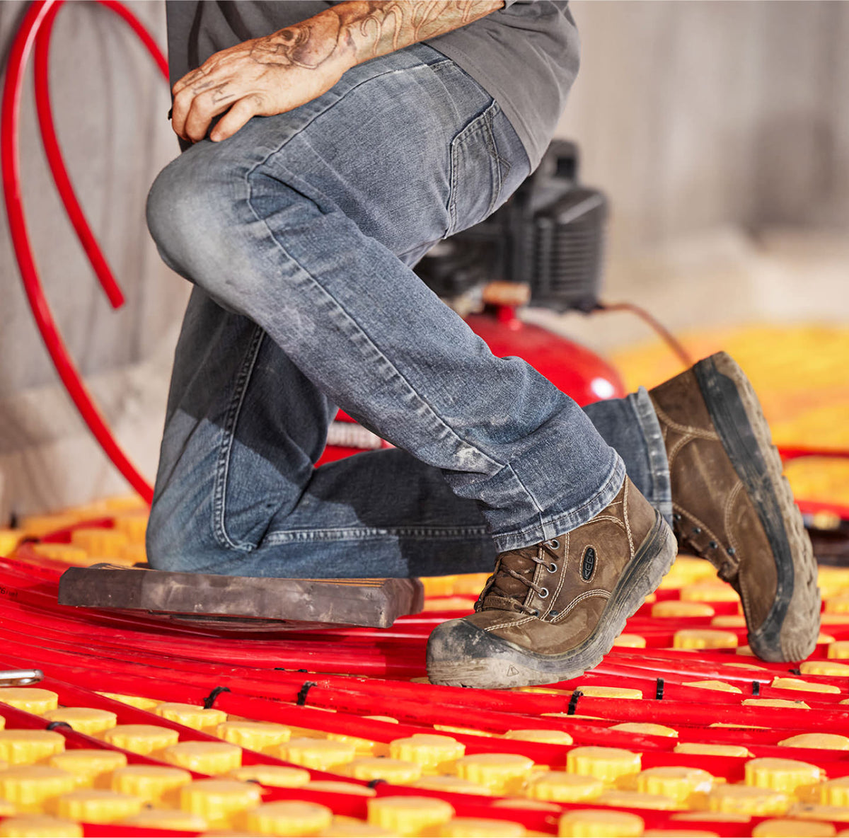 Waist down shot of man in jeans and Fort Wayne work boots working with red water pipes