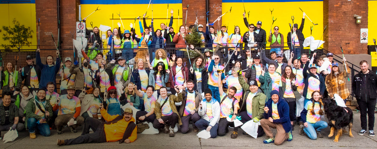 Keen Employees in tie-dye shirts posing with garbage-collecting supplies in front of Keen building