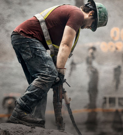A man working outside on a job site, using a large tool to drill into the ground.