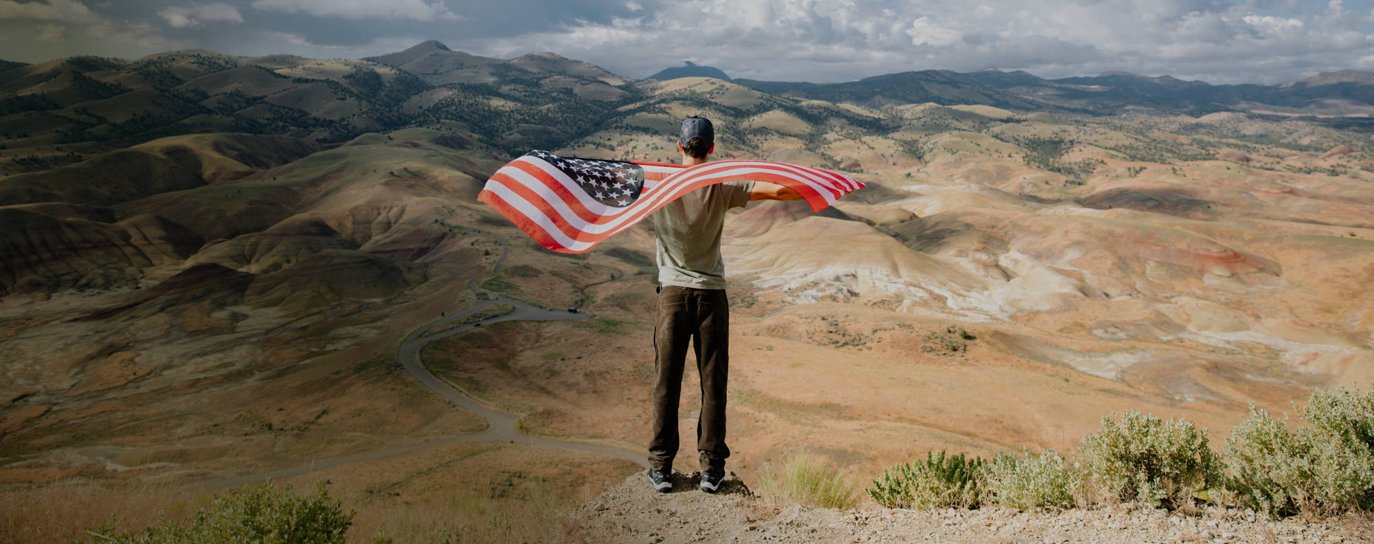 A person standing on a hill, with an American Flag flowing behind them.